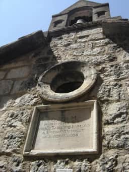 Stone church facade with an inscription and bell in Rose