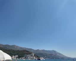 Bagnanti nell'acqua bassa di Bečići, con la costa della riviera che si incurva alle loro spalle.