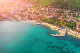 Veduta aerea o dall'alto dell'istmo che collega l'isola di Sveti Stefan alla terraferma, con la spiaggia pubblica sul lato nord e la Spiaggia della Regina su quello sud