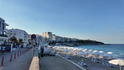 The promenade at Dobra Voda on a summer morning, cafés on one side and white parasols on the sand on the other