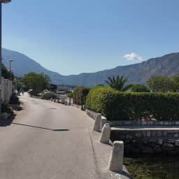 The coastal road along Dobrota's shore, following the water's edge with the bay and mountains beyond.