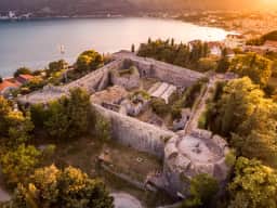 Aerial view of a ruined hilltop stone fortress above Herceg Novi, with the bay and the coast behind at sunset