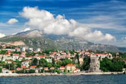 Vista panorámica de Herceg Novi desde el mar: el casco antiguo se eleva en terrazas desde la orilla, con murallas y campanarios recortados sobre el telón de fondo de las montañas