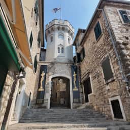La puerta de la torre del reloj Sahat Kula, entrada de piedra con arco al casco antiguo de Herceg Novi, con su esfera sobre el pasadizo.