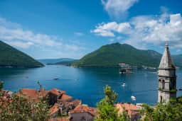 La promenade du front de mer de Herceg Novi, la forteresse Forte Mare en vue, les palmiers bordant le chemin et la baie qui s'étire derrière