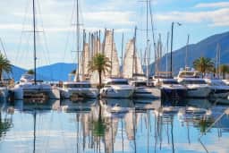 Marina Porto Montenegro u smiraj dana sa superjahtama, šetalištem uz obalu i planinama Bokokotorskog zaliva u pozadini