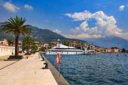 Vazdušna panorama Tivta sa marinom Porto Montenegro, šetalištem uz obalu i Bokokotorskim zalivom sa planinama u pozadini