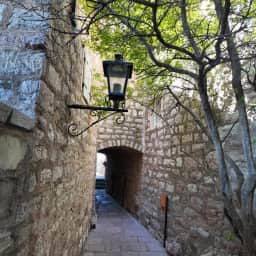 Pasaje de piedra con arco, lámpara y árboles dentro de Sveti Stefan