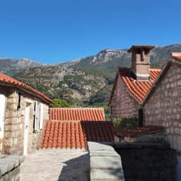 Cabañas de piedra y tejados de terracota en el interior de Sveti Stefan con las montañas Paštrovići detrás