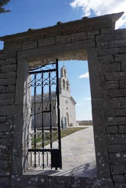 Die Nikolauskirche, eingerahmt von einem steinernen Torbogen in Žlijebi