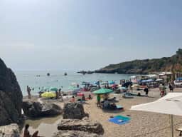 Rocks at the edge of Drobni Pijesak beach with bathers and parasols beyond