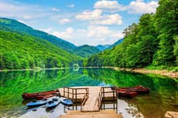 Дрвени чамци и кајаци поред мола на Биоградском језеру окруженом шумом