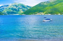 Small boat on sheltered blue bay water below mountains near Kamenari