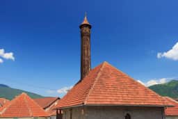 Stone mosque with red-tiled roof and a tall wooden minaret in Plav