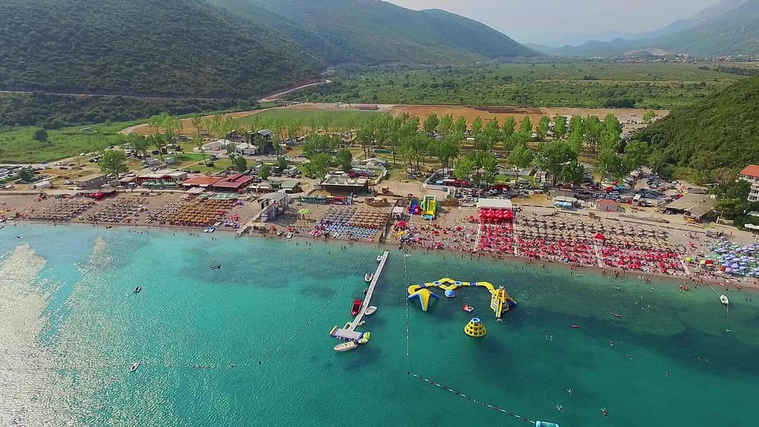 Aerial view of Jaz Beach showing turquoise waters, beach bars, and green mountains