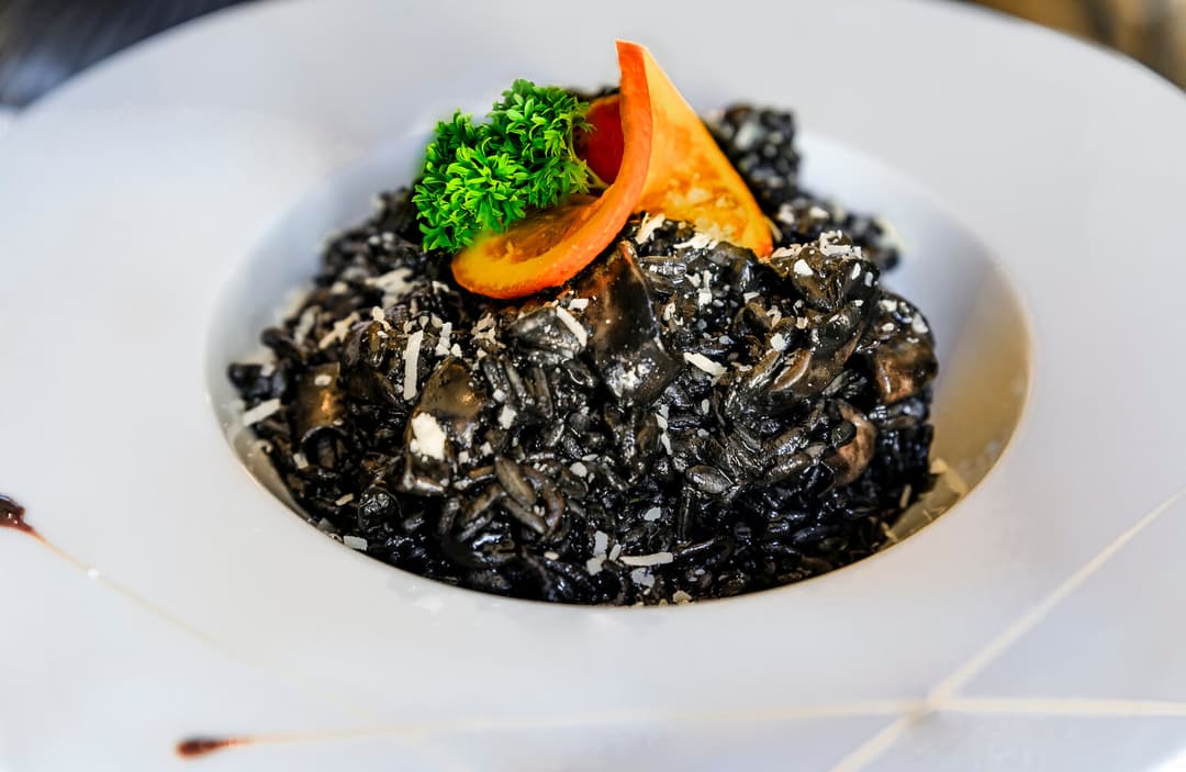 Plate of jet-black squid ink risotto garnished with parsley and tomato