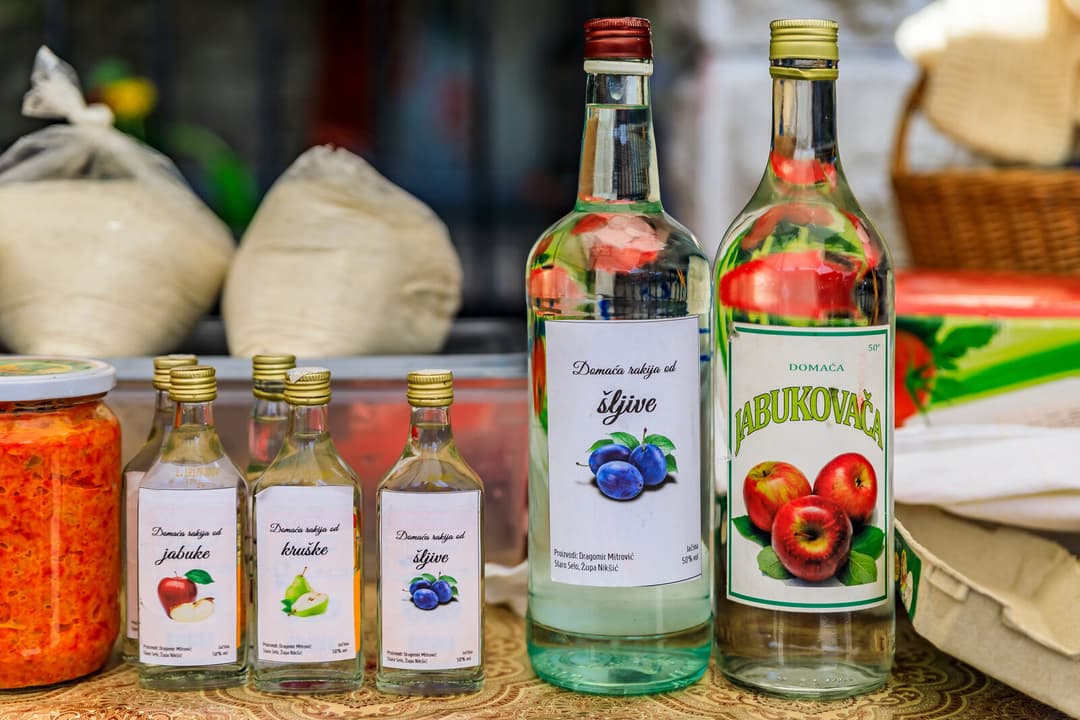 Selection of homemade rakija bottles with fruit labels on a rustic table