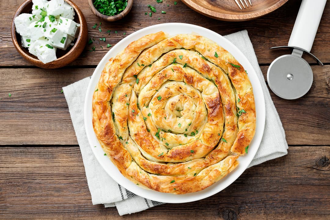 Golden spiral burek pastry on a white plate with feta cheese on the side