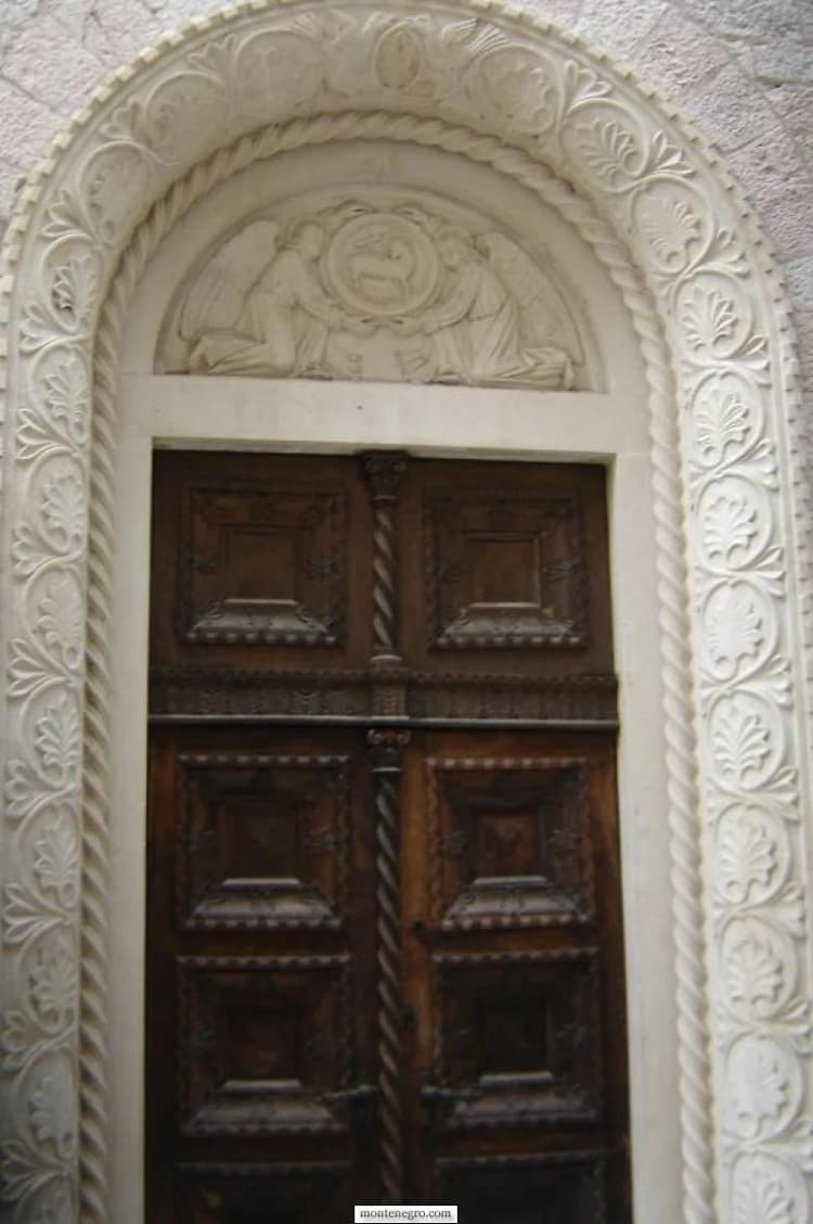 Portail de pierre en plein cintre richement sculpté et double porte en bois sombre à Kotor