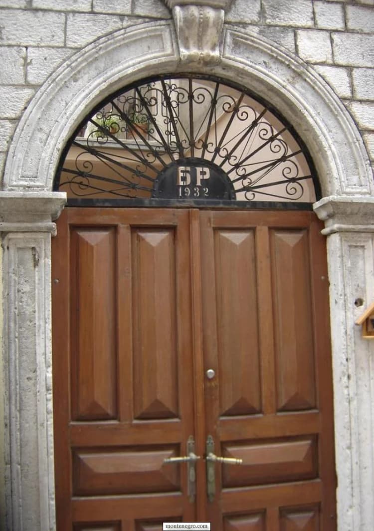 Porte à deux vantaux de bois surmontée d'une imposte en fer forgé en demi-cercle à Budva
