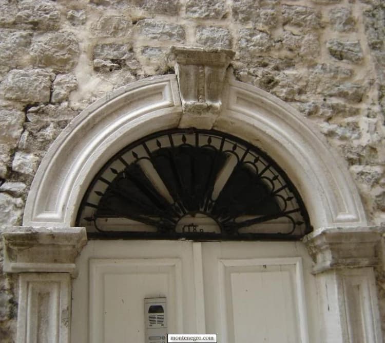 Porte à deux vantaux clairs sous un arc de pierre sculpté dans la vieille ville de Budva