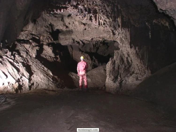 Caver using technical equipment inside a narrow limestone chamber