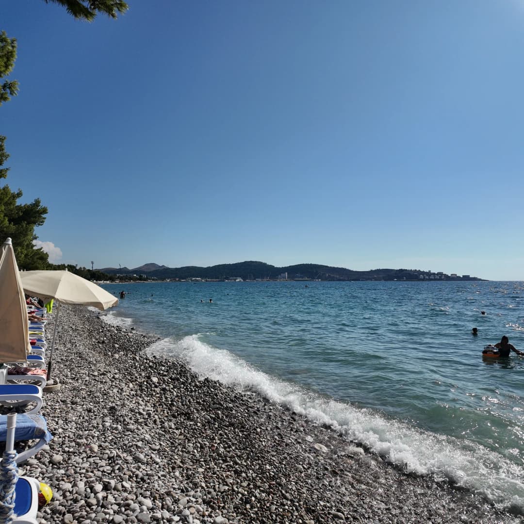 Šljunak, ležaljke i otvoreni zaliv na plaži Žukotrlica u Baru