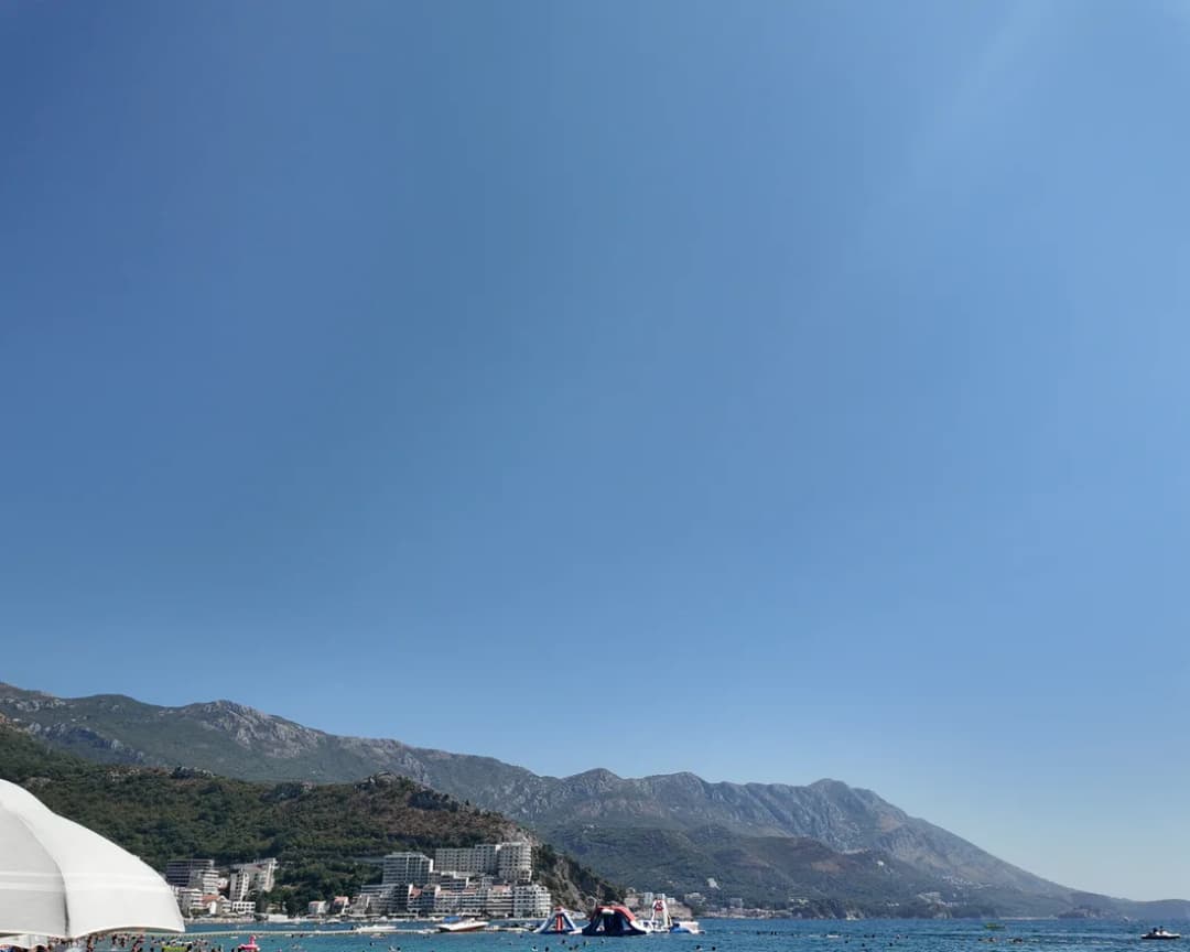 Swimmers in the shallows at Bečići with the riviera coastline curving away behind them.