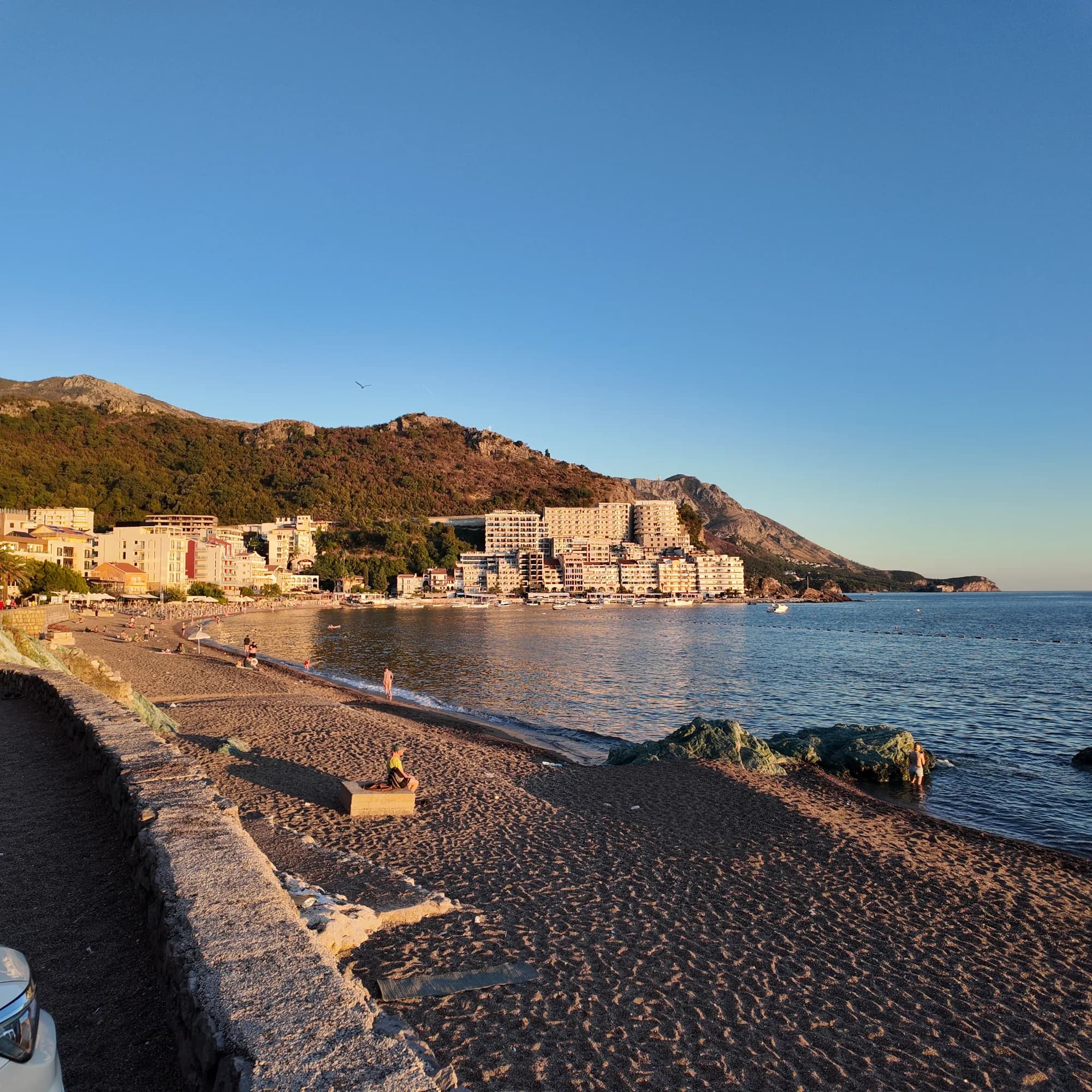 Evening on the Bečići sand from the promenade wall, looking east along the shore to the apartment blocks of Rafailovići