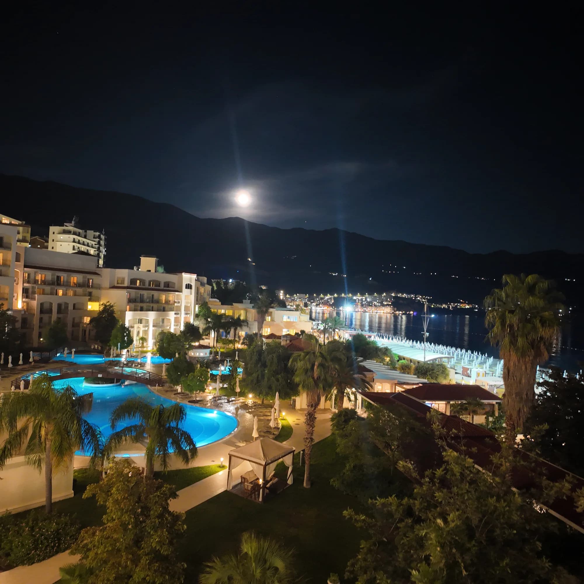 The Splendid’s pool lit blue at night, the hotel wings and the beach lights of Bečići beyond
