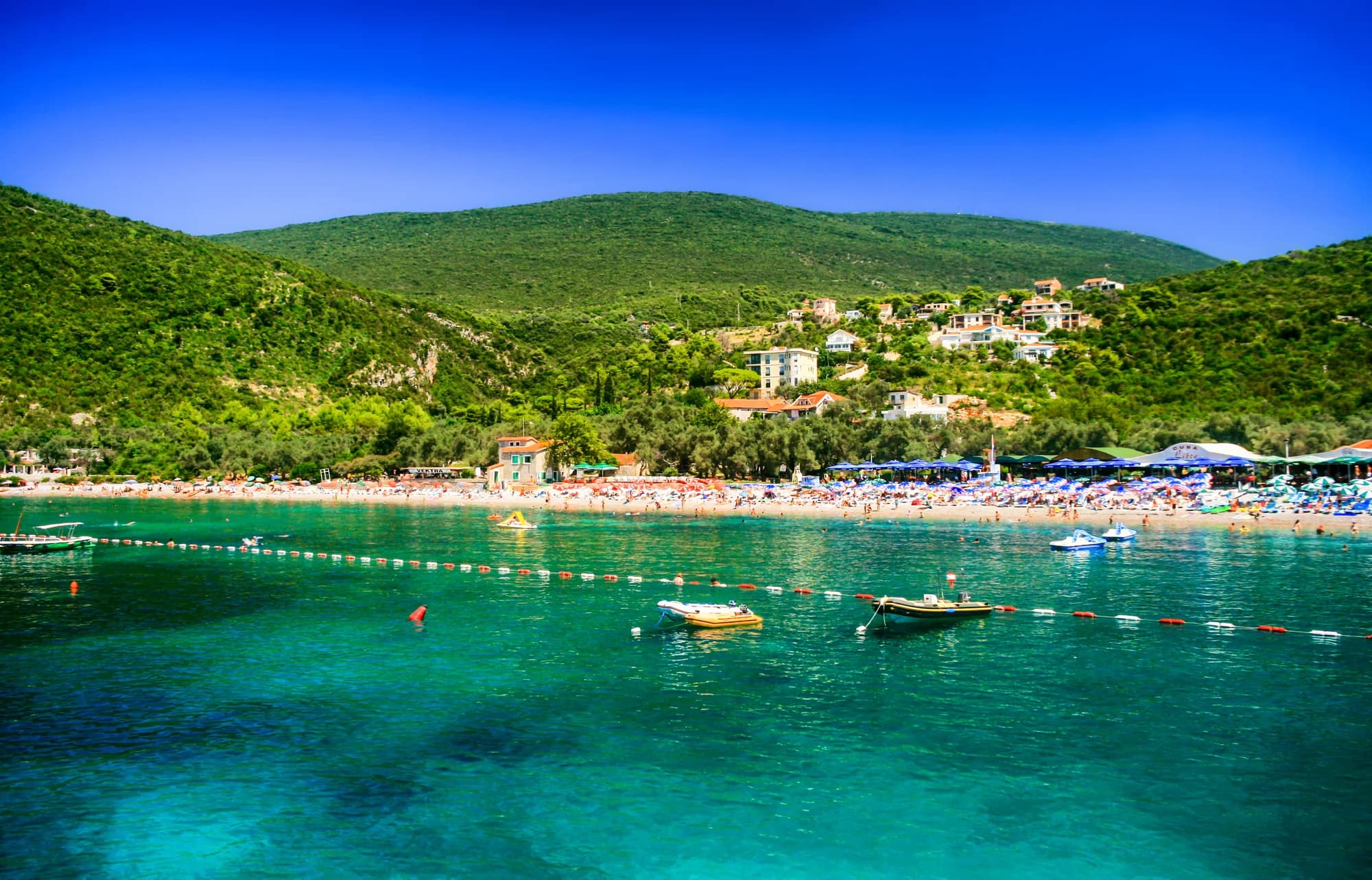 The pebble beach at Žanjice on a summer day, seen from the water — the busier neighbour ten minutes from Mirišta