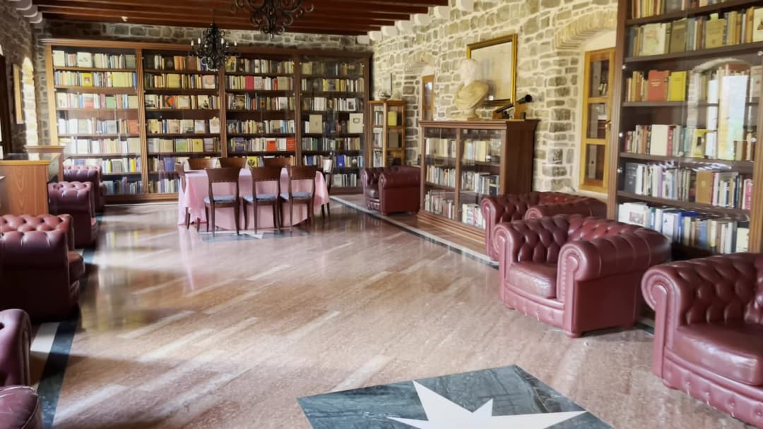 The reading room of Budva's municipal library: glazed bookcases against stone walls, oxblood leather armchairs and a marble floor.