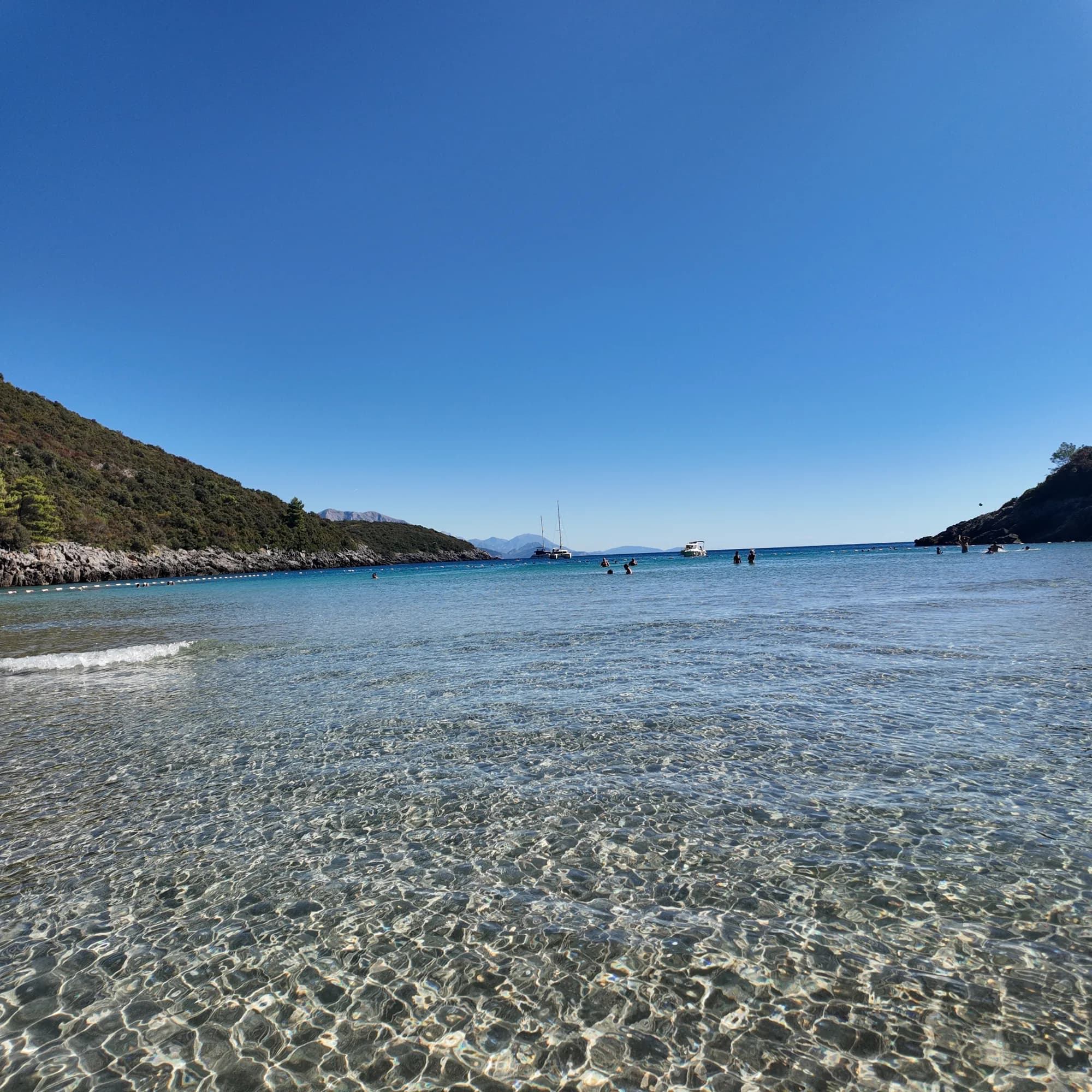 Knee-deep clear water over the sand-and-gravel bottom at Trsteno, the buoy line and yachts at the mouth of the cove