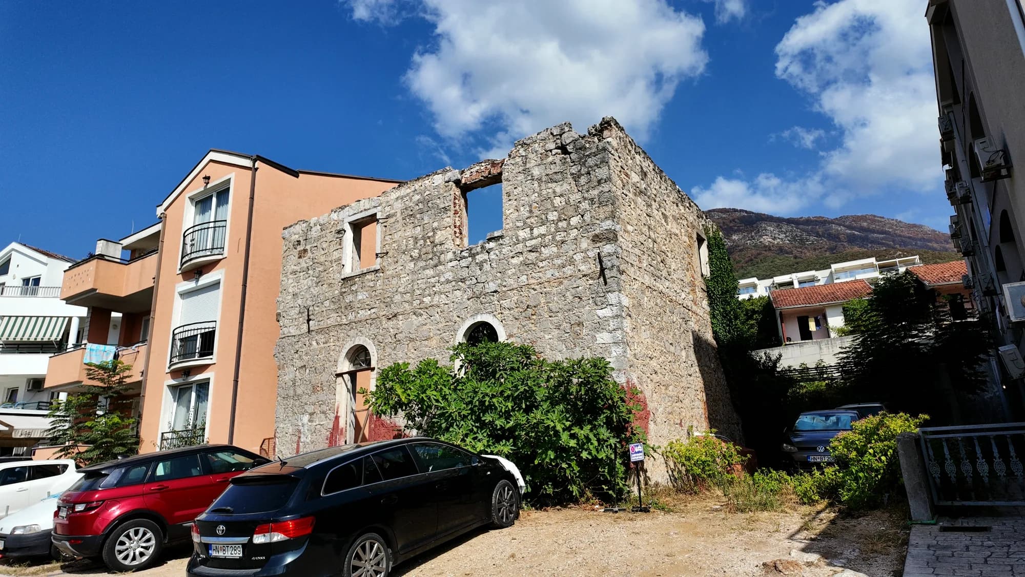 A roofless stone building standing between newer houses at Đenovići