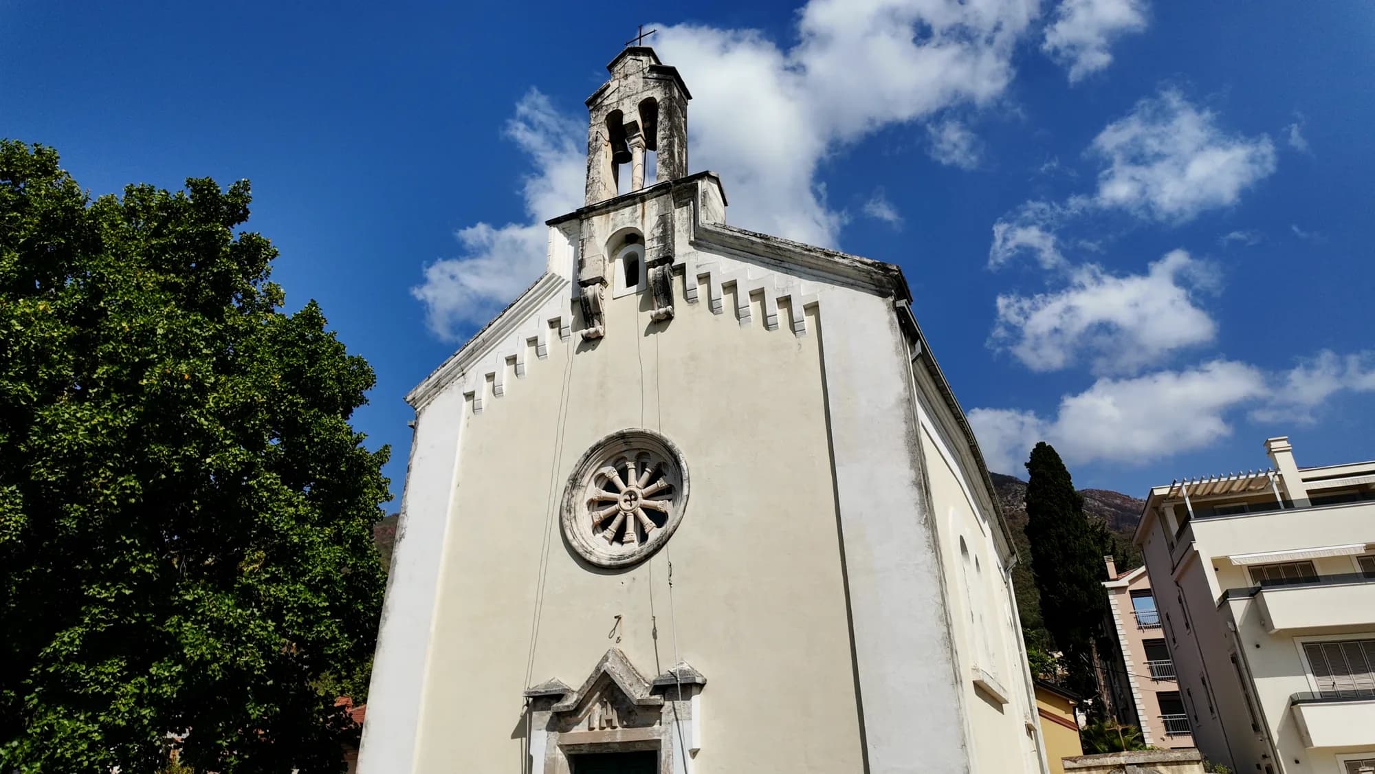 The parish church at Đenovići, its bell gable and rose window above the road