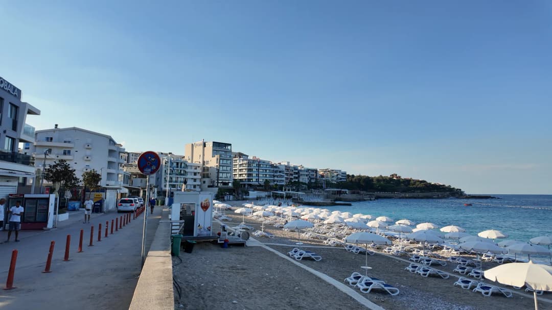 The promenade at Dobra Voda on a summer morning, cafés on one side and white parasols on the sand on the other