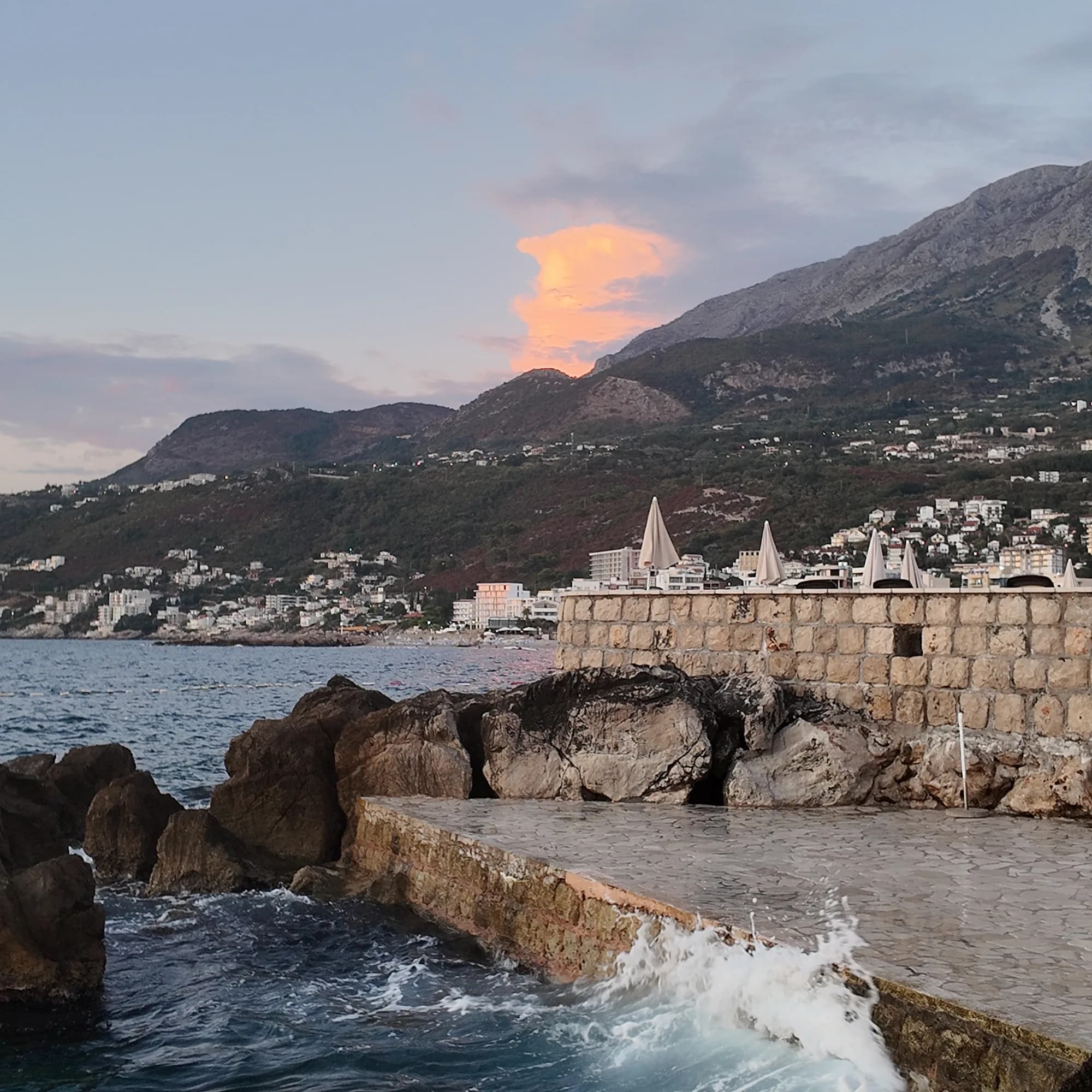 The hotel’s sea wall at dusk, a lit cloud above the hills over Dobra Voda