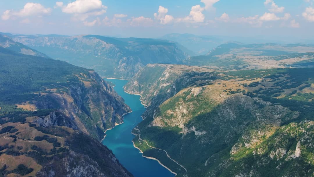 Širokougaoni snimak mosta Đurđevića Tara koji premošćuje kanjon, sa bandži skakačem usred slobodnog pada naspram dramatične pozadine kanjona