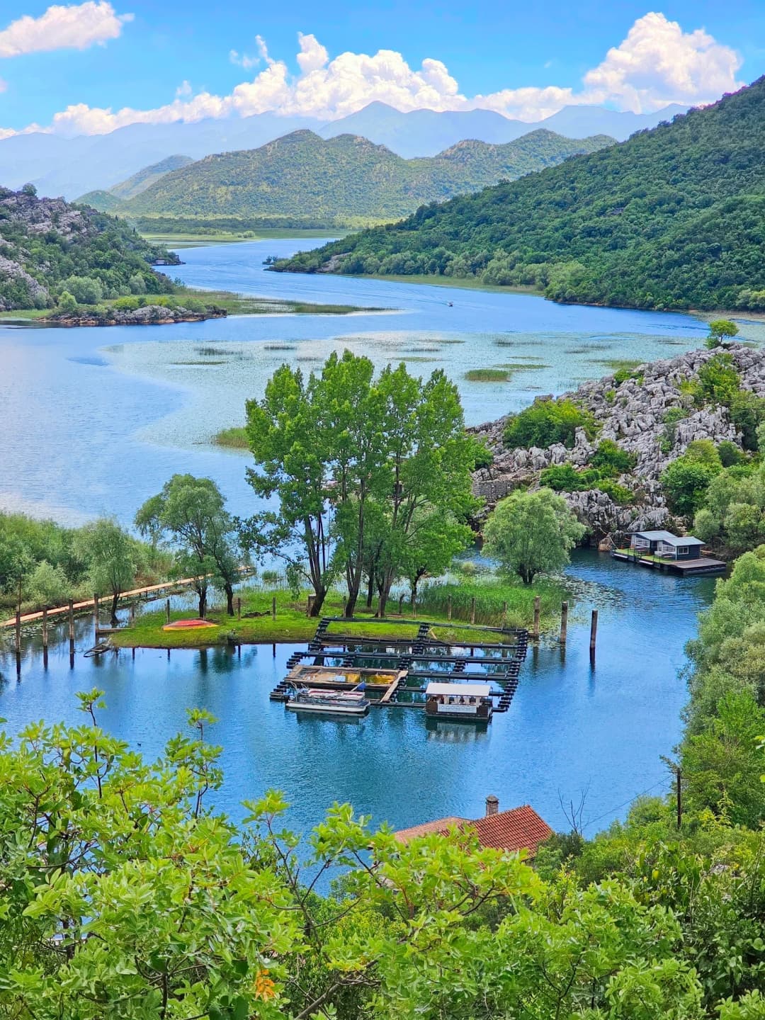 Duboko plavo Pivsko jezero viđeno sa staze na rubu kanjona, sa strmim liticama koje se spuštaju do vode i planinama u pozadini