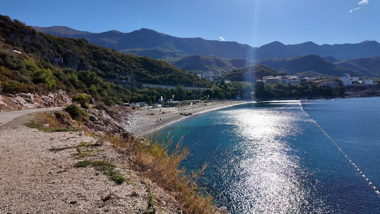 The full arc of Kamenovo beach from the coastal path on the Rafailovići side, buoyed bathing water and the hills of Pržno beyond