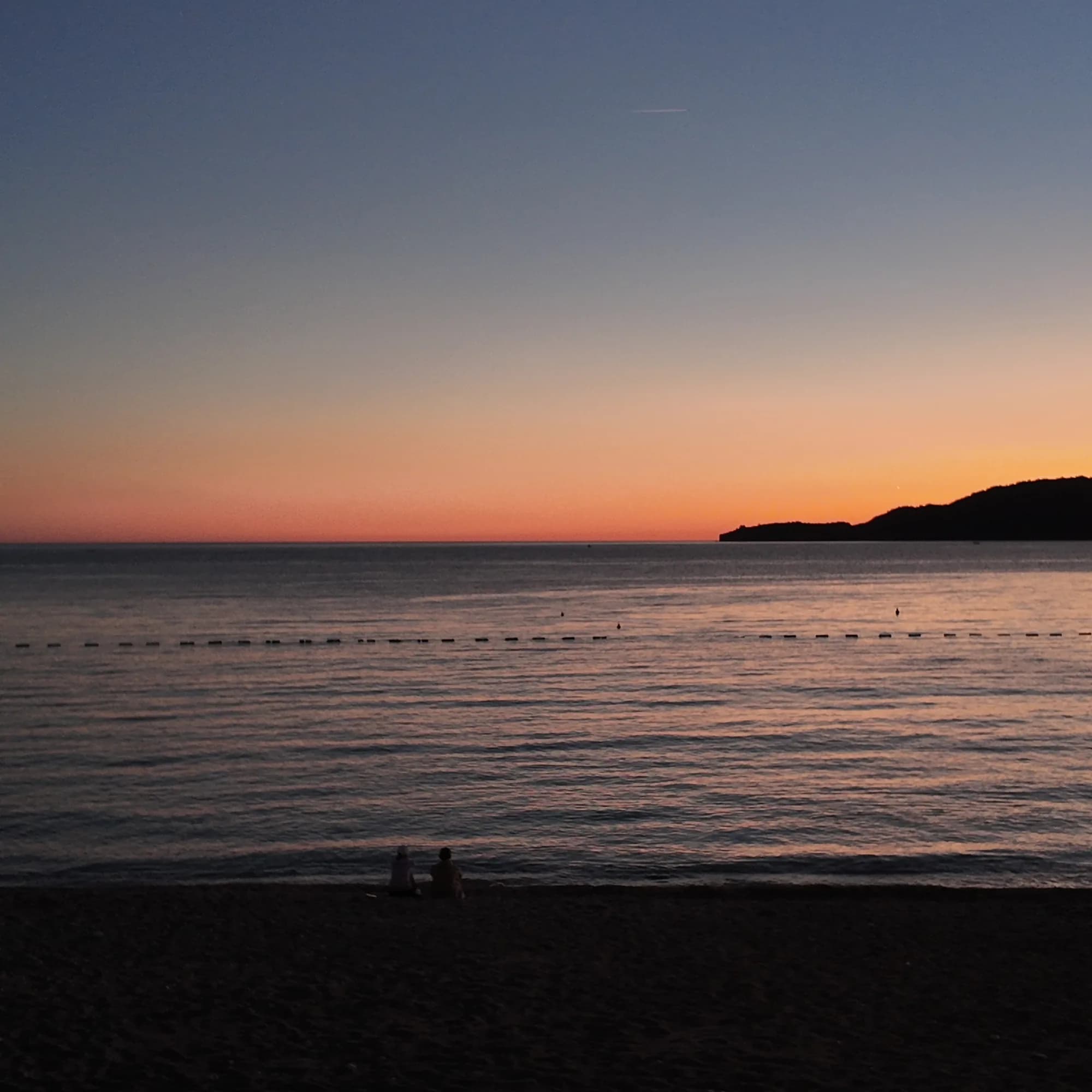 Sunset over the sea from the Kamenovo shore, the sky orange above the dark hills of the riviera