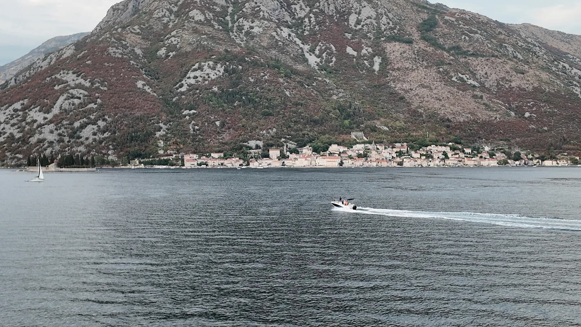 Perast strung along the foot of its mountain across the strait, a speedboat crossing