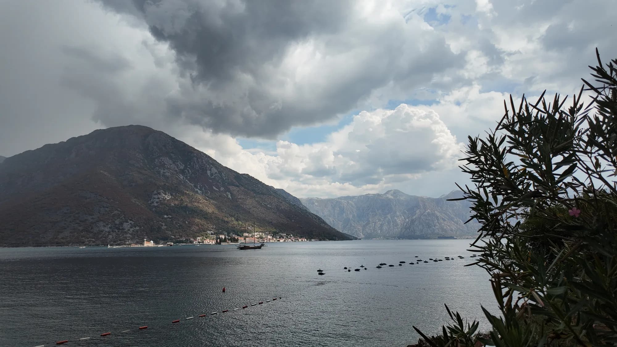 A storm cloud over Perast and the islet of Sveti Đorđe, seen from the Kostanjica shore through oleander