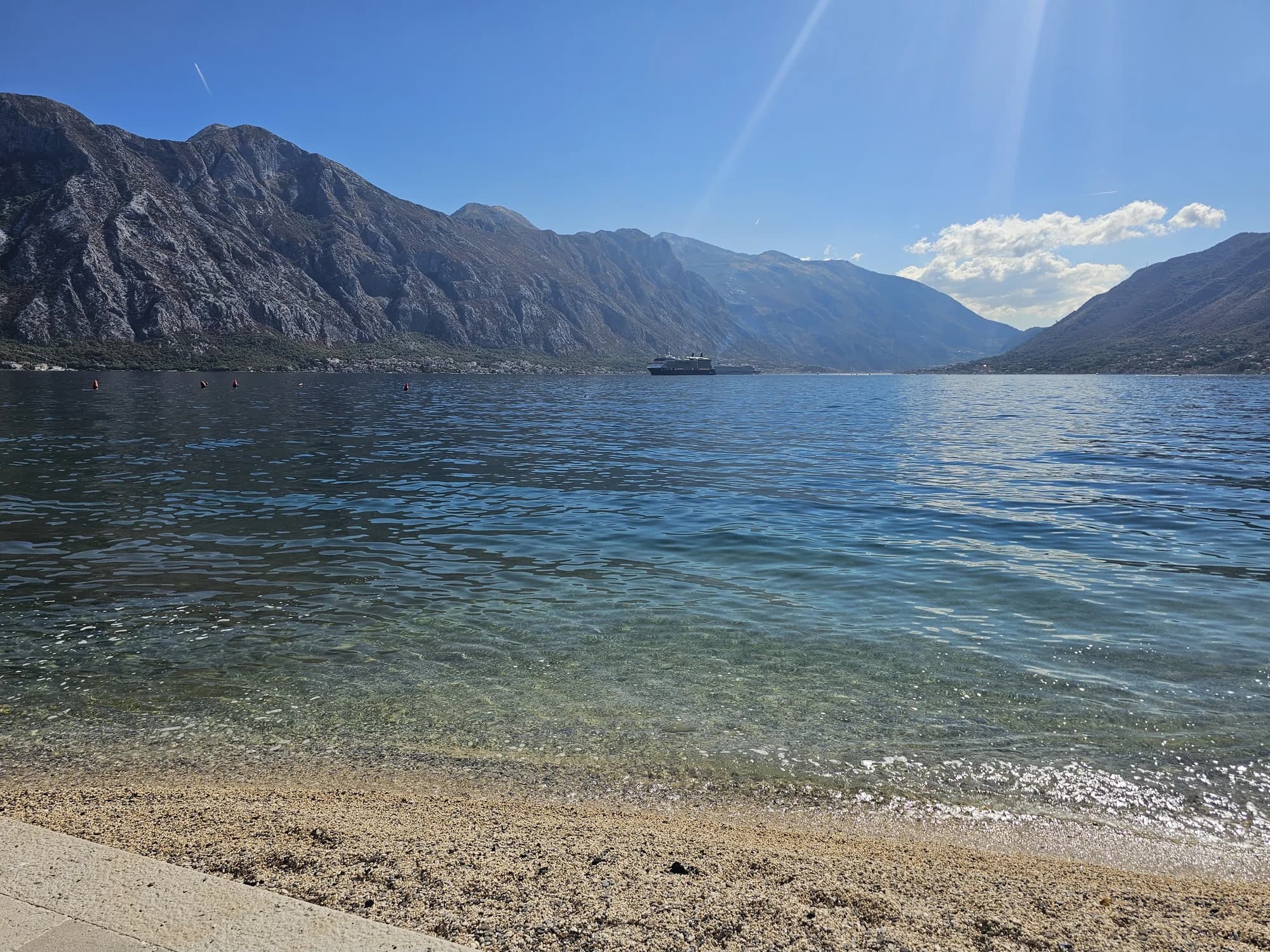 Clear water washing over the fine pebble shore at Bajova Kula, with the mountains of the inner bay beyond