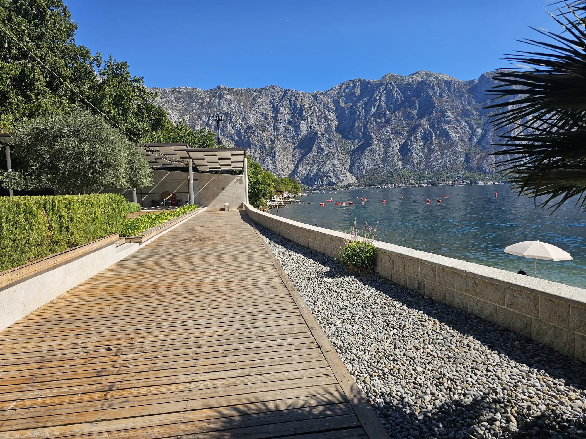 The landscaped timber deck at Bajova Kula beside the clear bay, with the mountains above Dobrota across the water