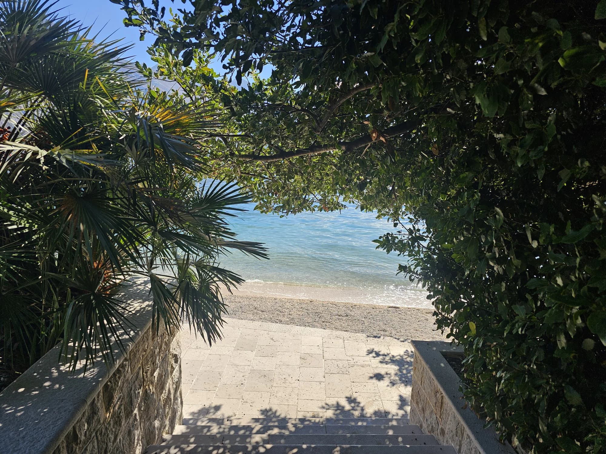 Stone steps through palms and leafy shade leading down to the pebble shore at Bajova Kula