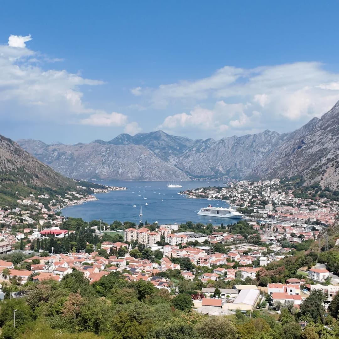 Wide panorama over the Bay of Kotor with the town spread along the shoreline beneath steep mountains.