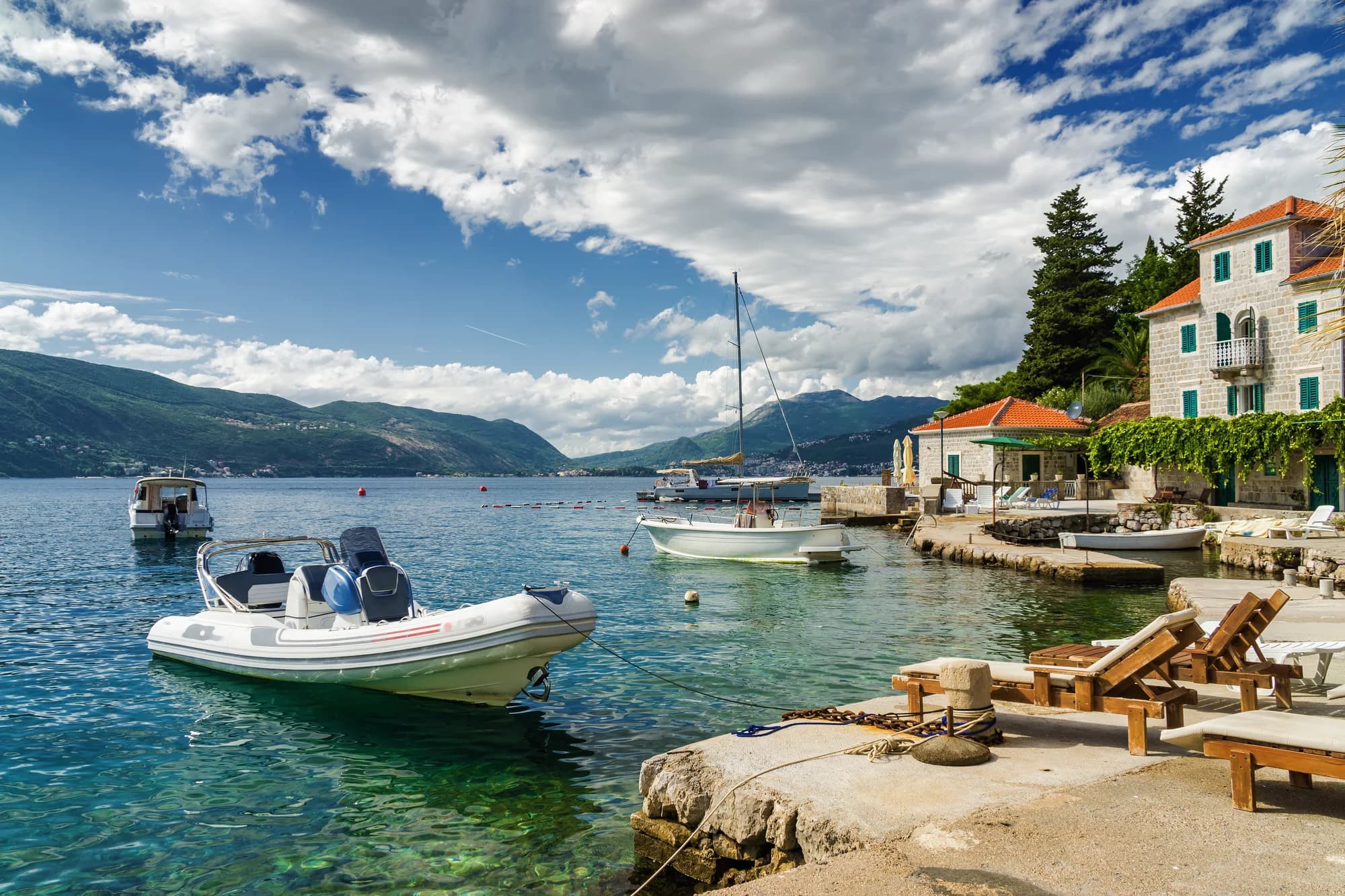 The quay at Rose, the village at the tip of Luštica: a rigid inflatable and a fishing boat below stone houses, loungers on the mole — the coves along this shore are reached from quays like this