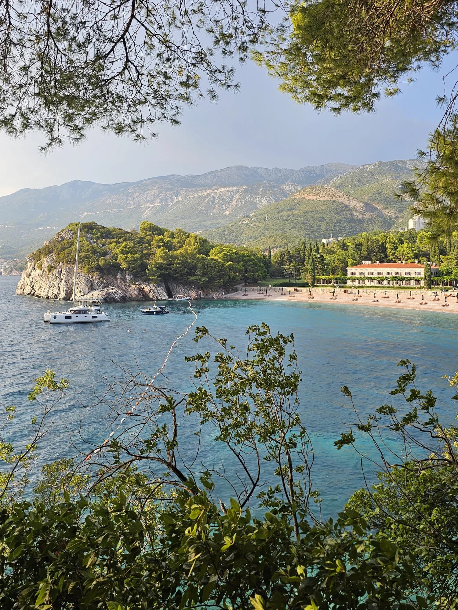 Miločer Beach and Villa Miločer across clear turquoise water, framed by pines on the rocky headland