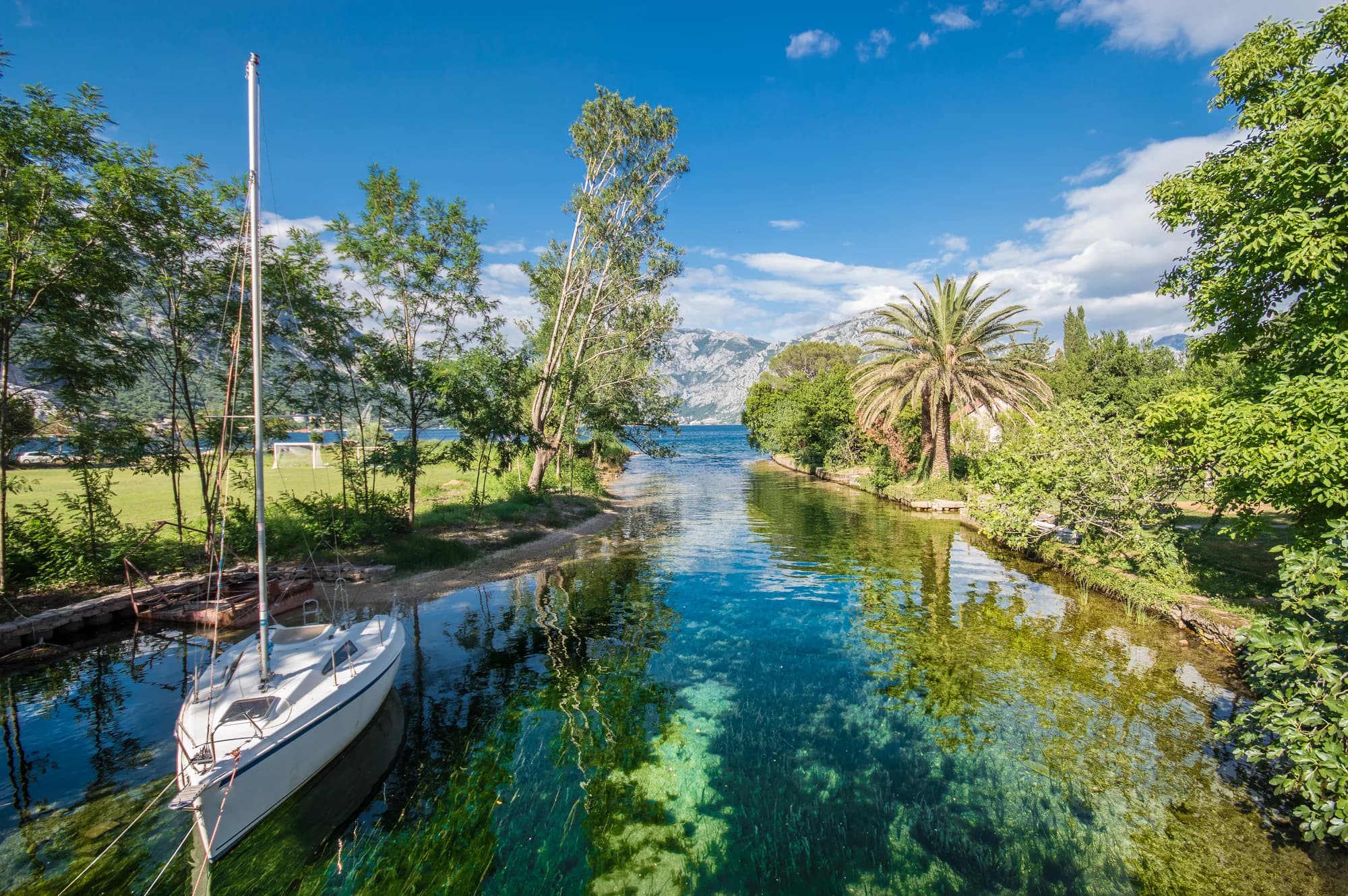 The clear millstream running out to the bay at Ćatovića Mlini, a sailing boat moored in it and the mountains of the far shore